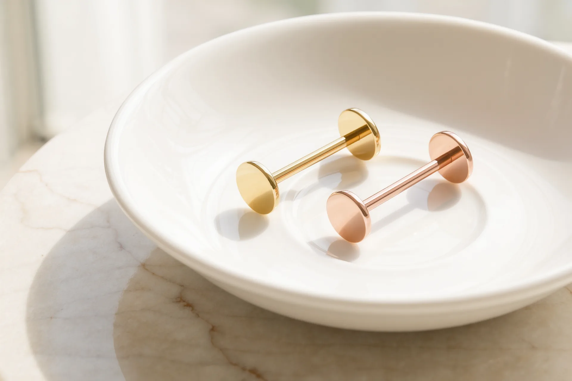 Massiver Barbell aus Roségold und Ring aus Gelbgold auf elfenbeinfarbener Seide neben einer Juwelierlupe.