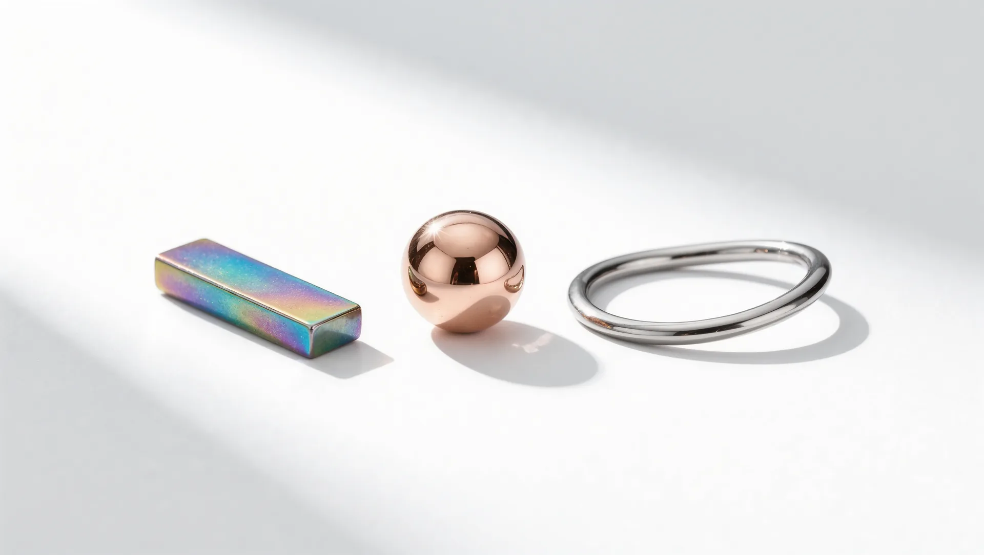 Anodisierter Titanstab in Blau, Violett und Gold neben einer Roségoldperle und einem Niobring auf weißem Grund